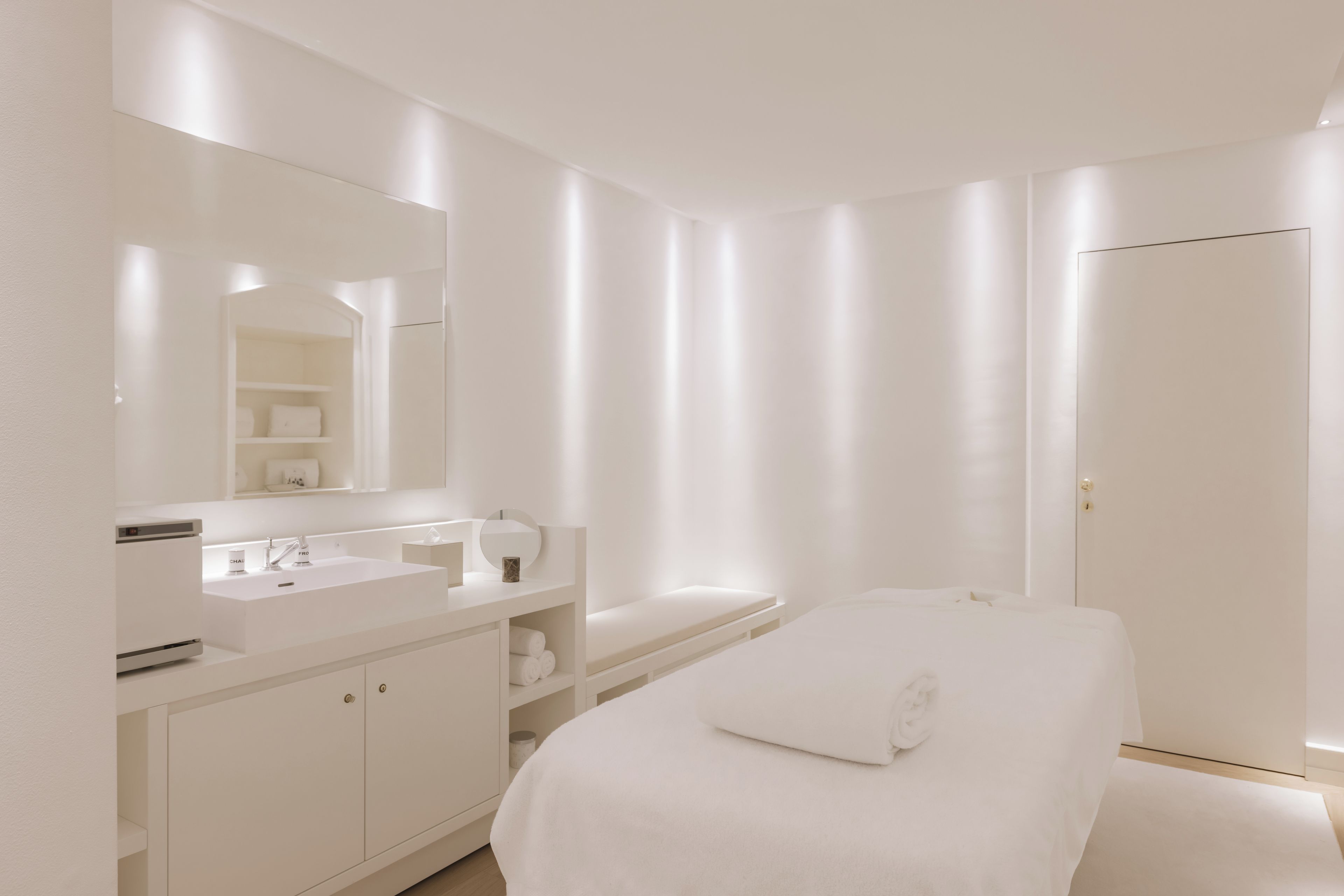 A modern bathroom with a large mirror, a white sink, and a towel on the floor.