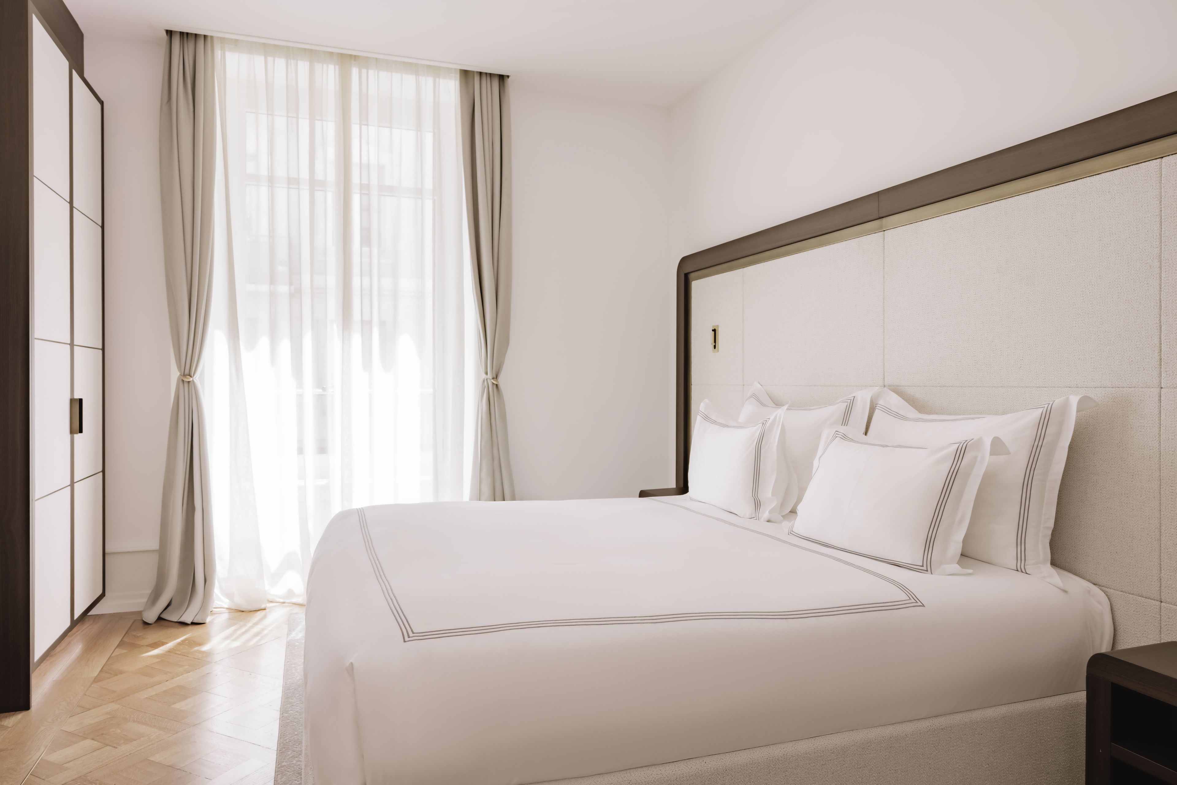 Una habitación de hotel con una cama grande, un armario y una ventana con cortinas.