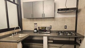 Uma cozinha compacta com pia, liquidificador, micro-ondas e fogão a gás.