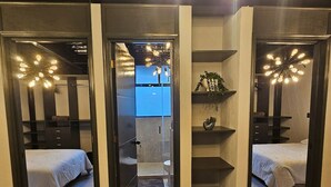 Quarto de hotel moderno com closet espaçoso, banheiro com chuveiro e cama com colcha branca.