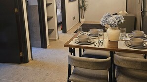 Uma sala de jantar com mesa posta para quatro pessoas, um lustre moderno e vista para um quarto.