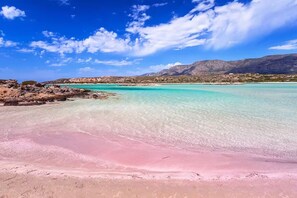A beach with clear turquoise water, pink sand, and distant mountains under a blue sky. - Dolonas Cozy House (Kisamos)
