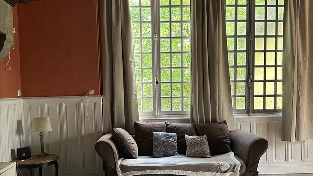 Une pièce chaleureuse avec un canapé marron, une petite table et une fenêtre avec des rideaux.