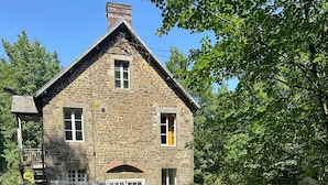 Un bâtiment en pierre avec un toit à pignon, une cour clôturée et une route dégagée devant.