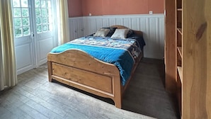 Une chambre avec un lit en bois, une fenêtre avec des rideaux, une armoire en bois et un plafond en pente.
