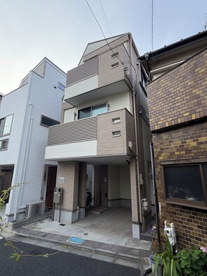 A multi-story residential building with a flat roof, a balcony, and a ground-level entrance. - Cozy 2-bedroom house in tranquil 渋谷区 with AC (Shibuyaku)