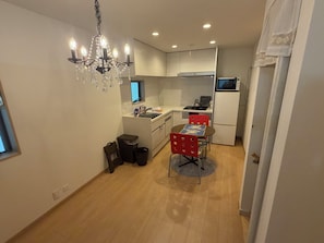 A compact kitchen with a chandelier, a dining table with chairs, a refrigerator, and a microwave. - Cozy 2-bedroom house in tranquil 渋谷区 with AC (Shibuyaku)