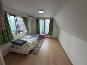 A small, tidy bedroom with a bed, a window with green curtains, a small bench, and an air conditioning unit. - Cozy 2-bedroom house in tranquil 渋谷区 with AC (Shibuyaku)