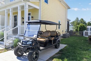 Ein Golfwagen vor einem Haus mit Veranda, Treppe und Briefkasten.