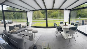 A modern, open-plan living area with a glass wall, a sofa set, a dining table, and chairs. - A beautiful and cozy vacation bungalow for up to 5 people on the Sonnwaldsteig (Kirn)