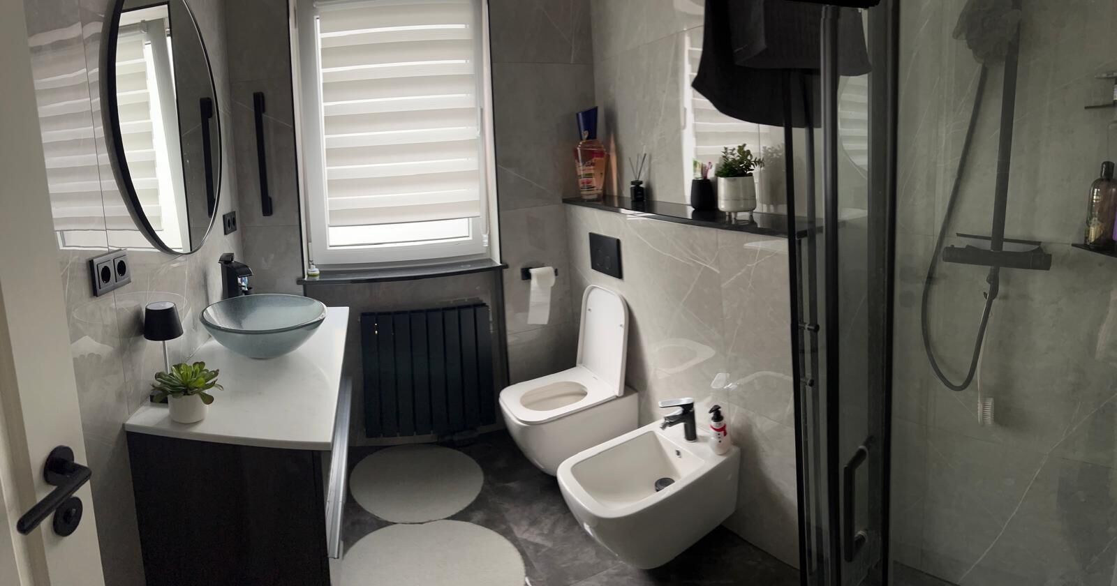 A modern bathroom with a toilet, bidet, sink, and a glass shower enclosure.