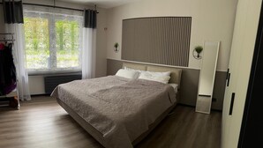 A modern bedroom with a large bed, a radiator, a window with curtains, a wall-mounted mirror, and a plant. - A beautiful and cozy vacation bungalow for up to 5 people on the Sonnwaldsteig (Kirn)