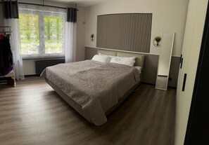 Ein modernes Schlafzimmer mit einem großen Bett, einem Heizkörper, einem Fenster mit Vorhängen, einem wandmontierten Spiegel und einer Pflanze.