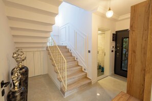 Un escalier avec une finition en bois, un luminaire moderne et une porte dotée d’un panneau de verre.