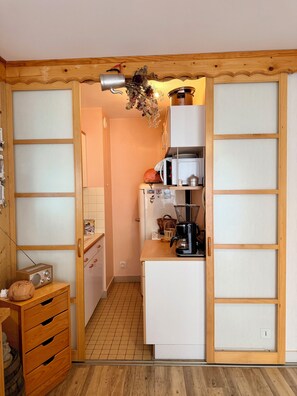 Eine kleine Küche mit Holzausstattung, einem Kühlschrank, einer Mikrowelle und einer Kaffeemaschine.