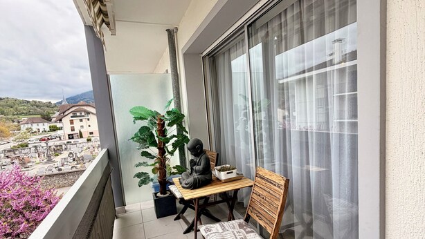 Un balcón con mesa y sillas, una planta en maceta y una estatua.