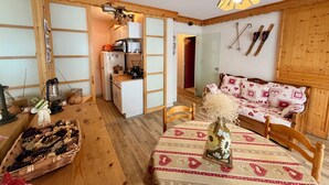 Una habitación acogedora con detalles de madera, una mesa de comedor con mantel estampado, un sofá con cojines decorativos y una zona de cocina con refrigerador y microondas.