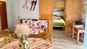 Una habitación acogedora con una cama de madera, una mesa de comedor y una silla. Hay esquíes y bastones de esquí en la pared, y un florero con flores sobre la mesa.
