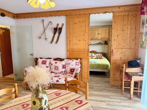 Ein gemütliches Zimmer mit einem Holzbett, einem Esstisch und einem Stuhl. An der Wand stehen Skier und Skistöcke, und auf dem Tisch steht eine Vase mit Blumen.