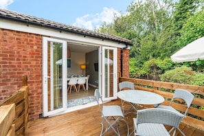 A patio with a table and chairs, a wooden fence, and a brick building with a glass door. - Downs Escape | By My Getaways (Lancing)