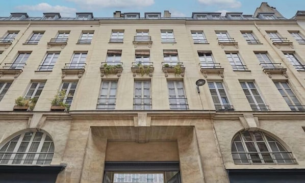 Ein mehrstöckiges Gebäude mit einer symmetrischen Fassade, großen Fenstern und einem zentralen Eingang mit einer dunklen Tür.