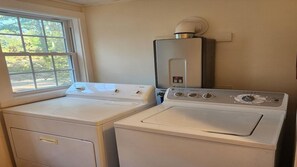 A laundry room with two washing machines and a dryer, a window, and a water heater. - Coastal Hideaway Retreat (York)