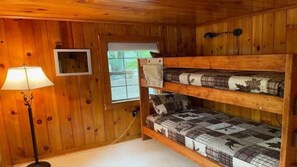 A bunk bed with a quilted mattress, a bedside lamp, and a window with a view of trees. - Coastal Hideaway Retreat (York)