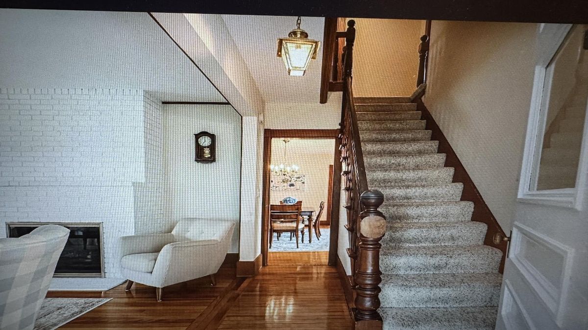 A staircase with wooden balusters leading to a landing, a white brick wall, and a clock on the wall.