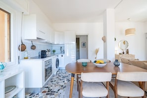 Eine moderne Küche mit weißen Schränken, einem eingebauten Backofen und einem Essbereich mit einem runden Holztisch und vier Stühlen.