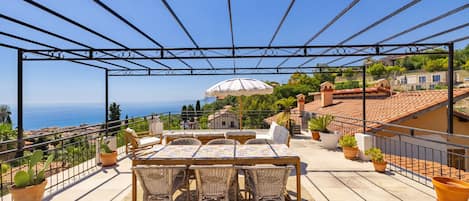 A terrace with a table and chairs, potted plants, and a view of the sea and buildings.