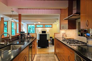 A modern kitchen with a central island, wooden cabinets, and a dining area with a black chair. - Private forest escape with creekside trails and firepit (Port Angeles)