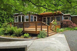 A wooden cabin with a deck, surrounded by lush greenery and a concrete pathway. - Private forest escape with creekside trails and firepit (Port Angeles)