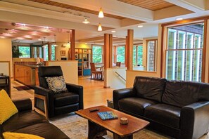 A spacious living room with a fireplace, a dining area, and a kitchen in the background. - Private forest escape with creekside trails and firepit (Port Angeles)