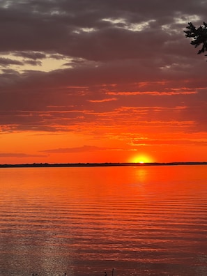 Un coucher de soleil sur une étendue d’eau calme, avec une silhouette de terre visible au loin.