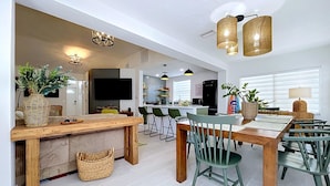 Une cuisine moderne avec un coin repas, comprenant une table en bois, des chaises vertes et un grand îlot central doté de tabourets de bar.