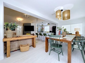 A modern kitchen with a dining area, featuring a wooden table, green chairs, and a large island with bar stools.