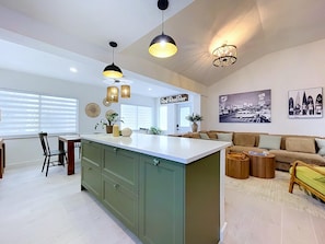 A modern kitchen with a central island, dining area with chairs, a sofa, and a coffee table.