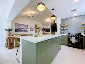 A modern kitchen with a central island, pendant lighting, and a large stove.