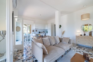 Ein modernes Wohnzimmer mit einem beigefarbenen Sofa, einer Küche im Hintergrund und einem gemusterten Boden.