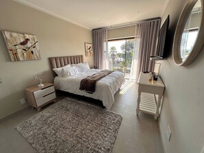 A bedroom with a bed, bedside tables, a TV, a window with curtains, and artwork on the walls. - Kalistas House Villa (Johannesburg)