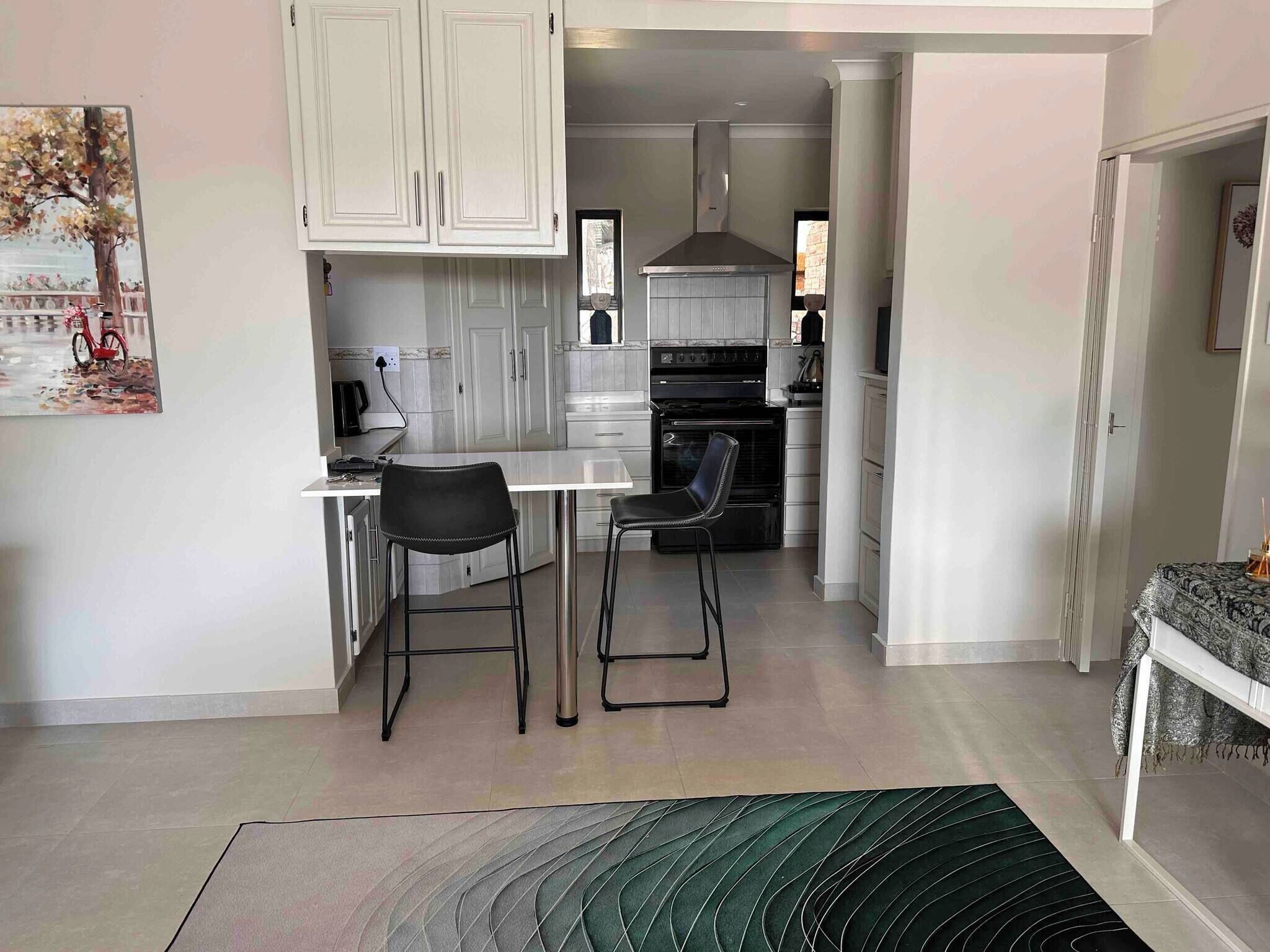 A modern kitchen with white cabinets, a black stove, and a dining area with two chairs.