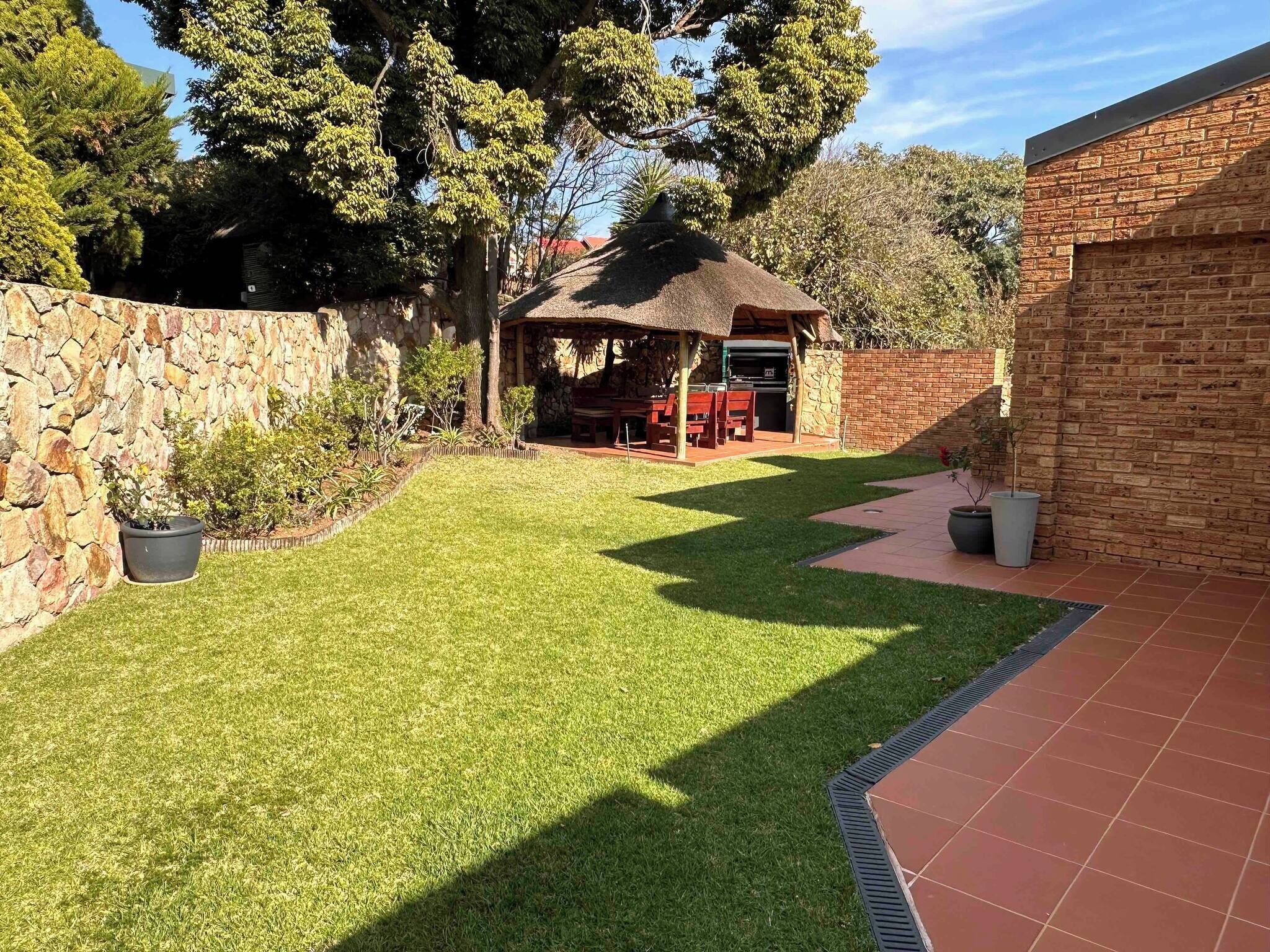 A well-maintained backyard with a stone wall, a grassy lawn, a barbecue area, and a brick building.