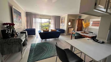 A modern living room with a sofa, a dining table, and a kitchen area.