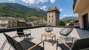 A terrace with outdoor seating, a stone tower, and a mountainous backdrop.