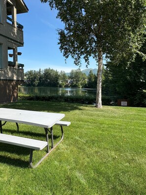 A picnic table in a grassy area with a lake and trees in the background. - A relaxing and inviting retreat in the Reflection Lake area of UMED. (Anchorage)
