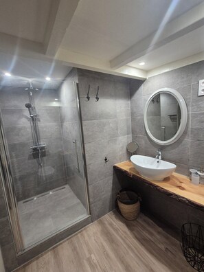 Ein modernes Badezimmer mit einer in Glas abgeschirmten Dusche, einem hölzernen Waschtisch mit weißem Waschbecken und einem runden Spiegel.