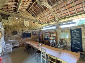 Un intérieur rustique avec un mur en pierre, un plafond en bois, une longue table en bois et une bibliothèque.