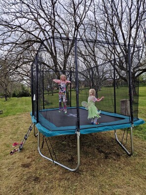 Ein Trampolin in einer Gartenanlage, im Hintergrund Bäume.