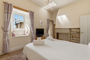 A bedroom with a bed, a television, a window with curtains, a fireplace, and a stone wall. - Ghyllstead - North East Escapes (Glanton)
