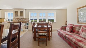 A dining area with a table and chairs, a sofa, and a view of the outdoors through large windows. - Ghyllstead - North East Escapes (Glanton)